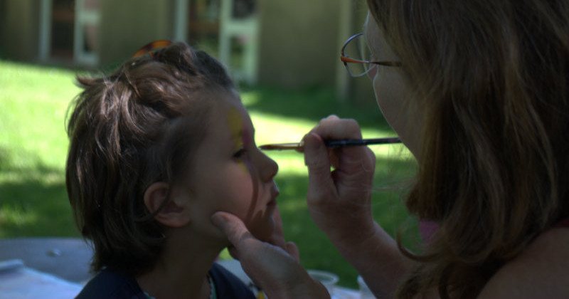 Une adulte maquille le visage d'un enfant au pinceau
